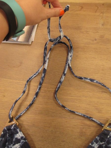 The double string wraps behind your neck, threads through the triangles, then ties in a single-string knot behind the neck.
